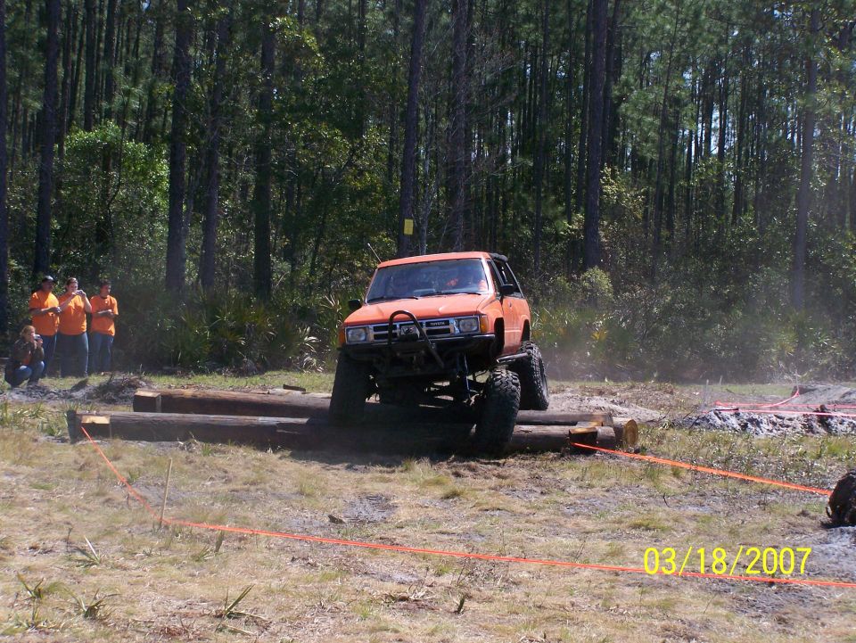 Orange off-road SUV with lifted suspension driving over logs