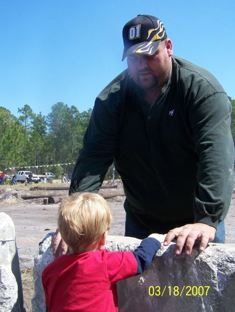 1989 Ford Bronco - Man and child interact near rocks, with trucks in the background on a sunny day.