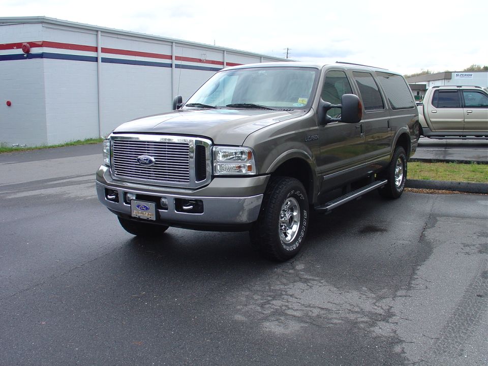 Tan Ford Excursion SUV, front 3/4 view with chrome grille and wheels, parked outside a building.