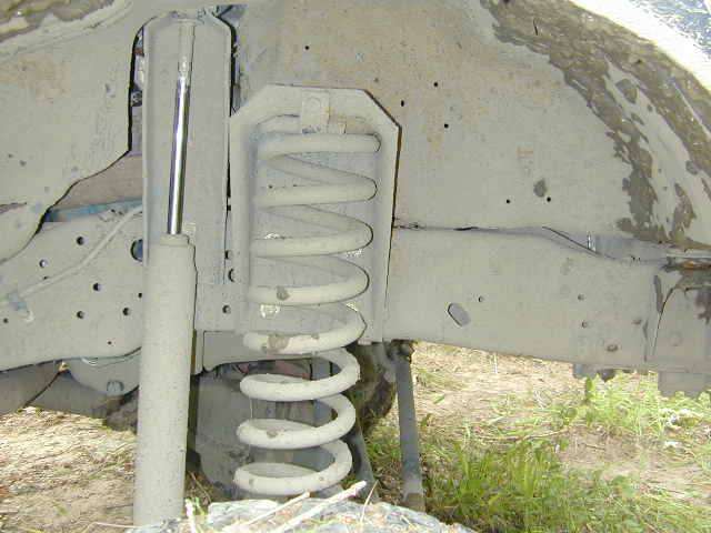 Mud-caked coil spring and shock absorber under a vehicle frame rail