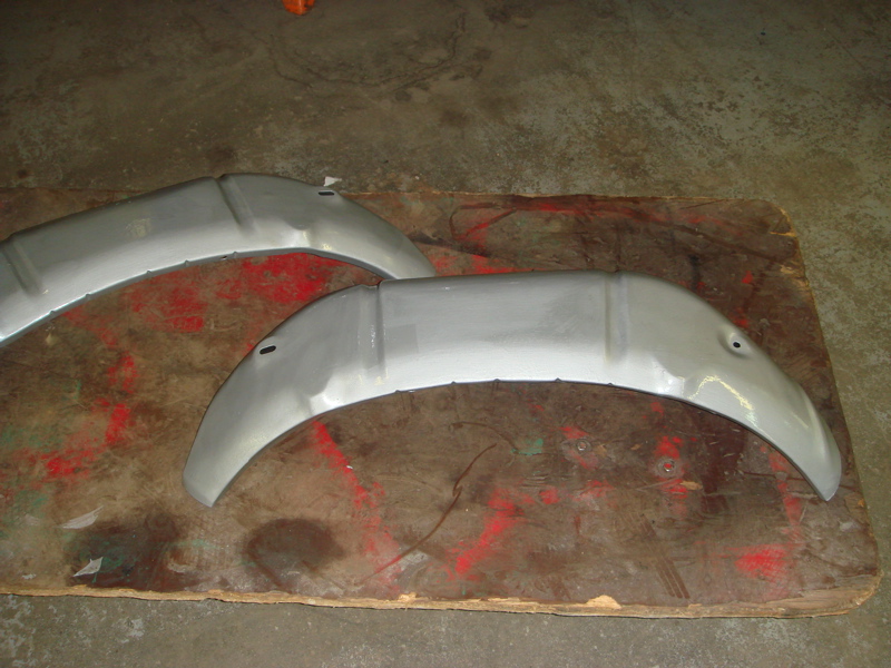 Two unpainted metal inner fender sections on a wooden board