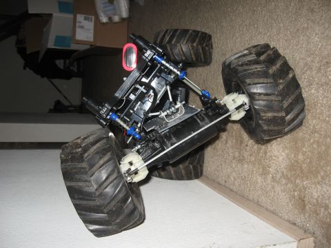 1990 Ford Bronco - An RC monster truck chassis with the body shell removed, sitting on a carpeted step and showing its four large knobby tires, long-travel co…