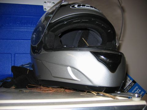 1985 Ford LTD Crown Victoria - A silver motorcycle helmet sits on a shelf next to gloves and pine needles, with a blue cooler behind it.