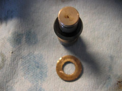1985 Ford LTD Crown Victoria - A disassembled metal component and a washer are shown on a textured surface, possibly during a repair or maintenance process.