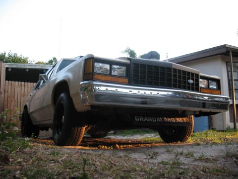 1985 Ford LTD Crown Victoria - This 1980s Ford sedan features a prominent chrome bumper and a distinctive black grille, seen from a low front angle.