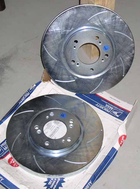 1996 Ford Probe - Two slotted brake rotors are shown resting on a USPS Priority Mail box.