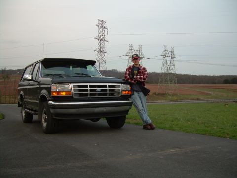 1992 Ford Bronco - A black 1992 Ford Bronco is parked on a paved surface with a man leaning against its front fender.