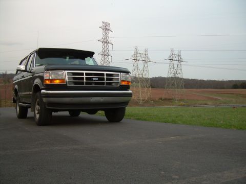 1992 Ford Bronco - 1992 Ford Bronco parked on asphalt with power lines and fields in the background.