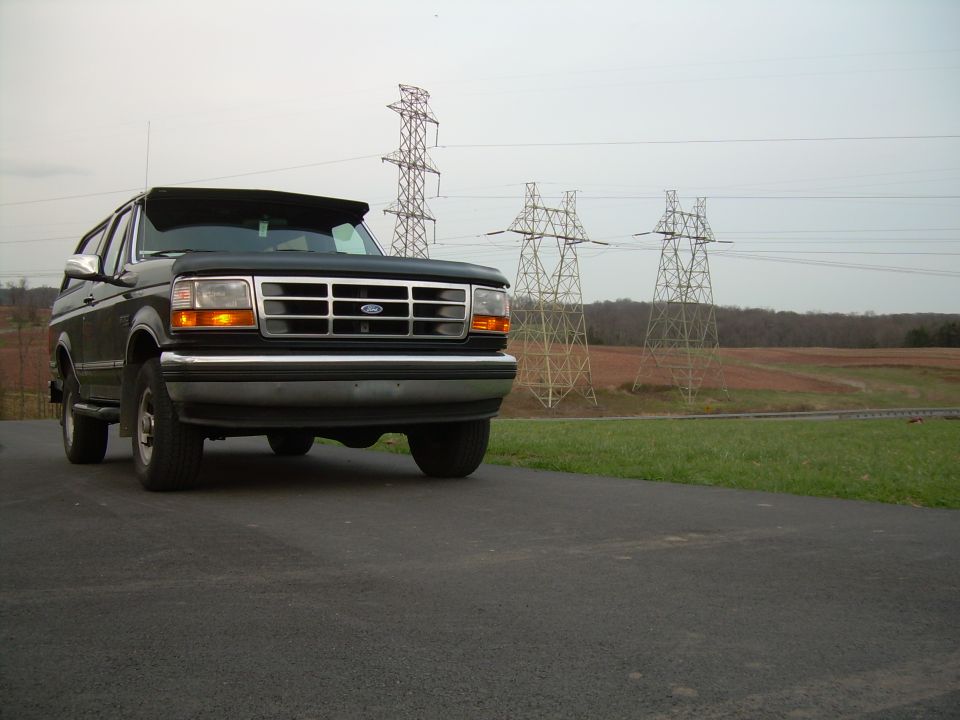 1992 Ford Bronco parked on asphalt, power lines and fields behind it