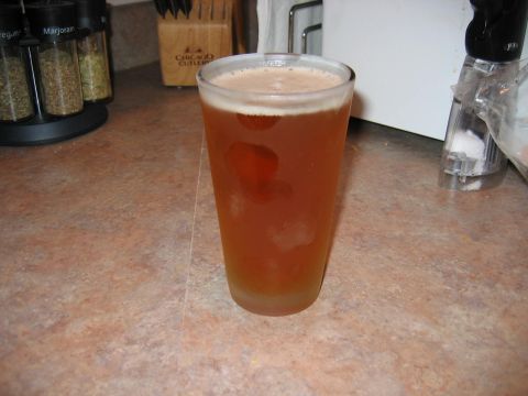 1985 Ford LTD Crown Victoria - A glass of amber beer with a frothy head sits on a speckled countertop, with spice jars and a knife block in the background.