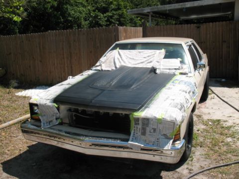 1985 Ford LTD Crown Victoria - A car is being prepped for painting, with the hood covered in primer and the fenders masked off.