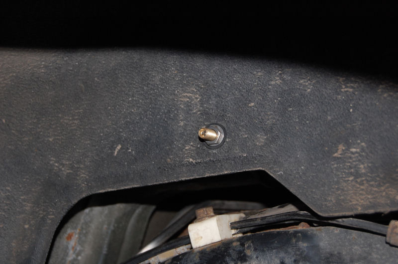 Close-up of an air valve stem mounted on a dark, textured vehicle frame component