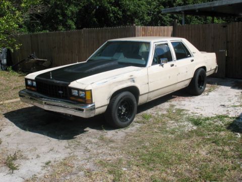 1985 Ford LTD Crown Victoria - This older model sedan has a matte black hood and black steel wheels.
