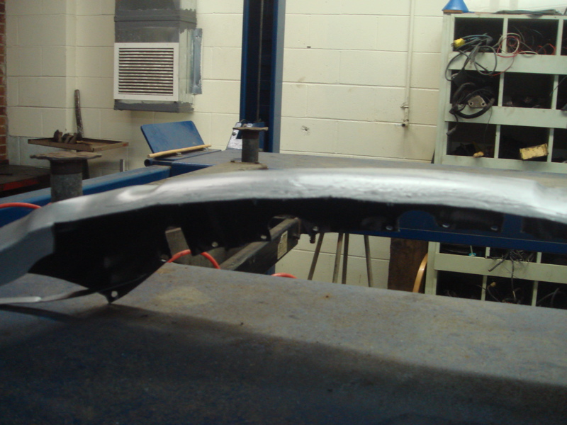 close-up of a curved metal car body panel on a lift, showing some repair work