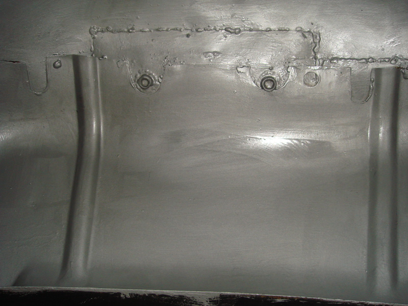 Close-up of a metal inner fender with visible welds and bolt holes