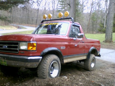 1989 Ford Bronco - Red 1989 Ford Bronco parked off-road with a roof rack four smiley face lights.