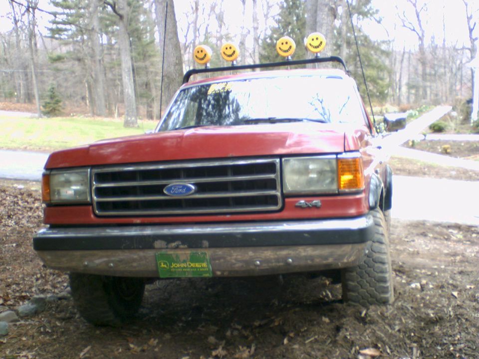 Front view of a red Ford pickup with a John Deere plate and smiley face lights on the roof rack