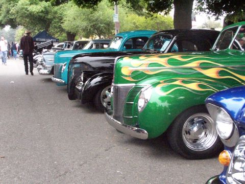 1990 Ford Bronco - A row of classic cars, including a green hot rod with flame decals, are displayed at a car show.
