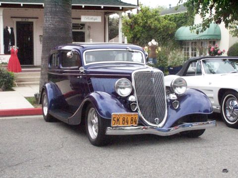 1990 Ford Bronco - Purple 1934 Ford hot rod sedan with custom wheels and California plates parked next to a white convertible.