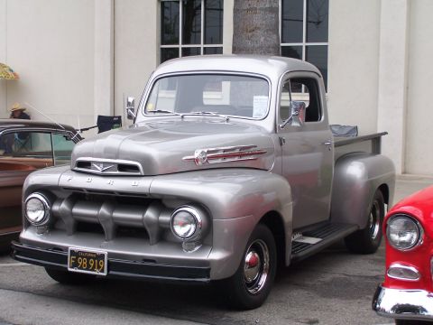 1990 Ford Bronco - A silver 1951 Ford F-1 pickup truck is parked next to other vehicles at an outdoor car show.