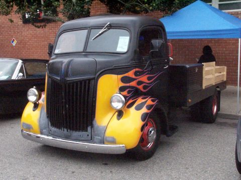 1990 Ford Bronco - A vintage flatbed truck with custom flame paint is displayed at an outdoor event.