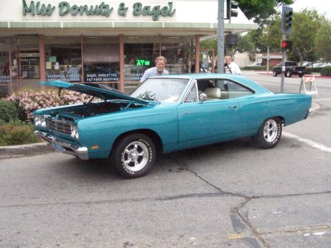1990 Ford Bronco - A teal 1969 Plymouth Road Runner coupe is displayed with its hood up in front of a donut shop.
