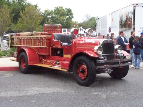 1990 Ford Bronco - A vintage red fire truck with a wooden ladder is parked on a street, with people in the background.