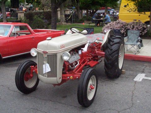 1990 Ford Bronco - A vintage Ford tractor is displayed at a car show next to a red pickup truck.