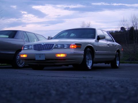 1996 Mercury Grand Marquis - Two sedans sit parked on asphalt under a cloudy sky at dusk.
