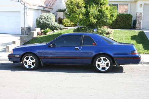 1987 Ford Thunderbird - A blue 1987 Ford Thunderbird Turbo Coupe is seen from the side in front of a house.