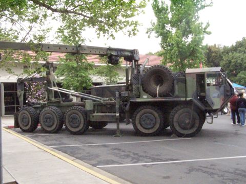 1990 Ford Bronco - A large military tow truck with an extended crane arm is parked in a lot, showing its side profile and camouflage paint scheme.