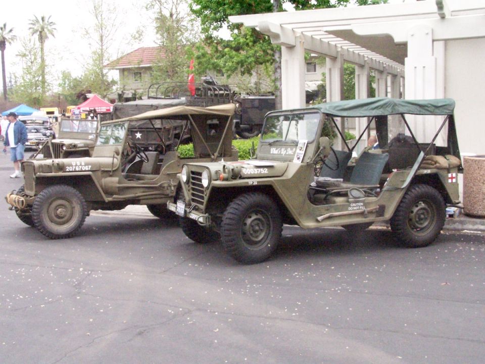 Two olive drab military jeeps parked side-by-side. The one on the left has 'USA 20767067' on its side. The one on the right has '0003752' and 'What's Up, Doc?' on its side