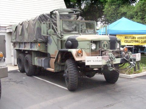 1990 Ford Bronco - Military truck with camouflage tarp over bed, SPT VIICAV plate on front bumper, parked outdoors.