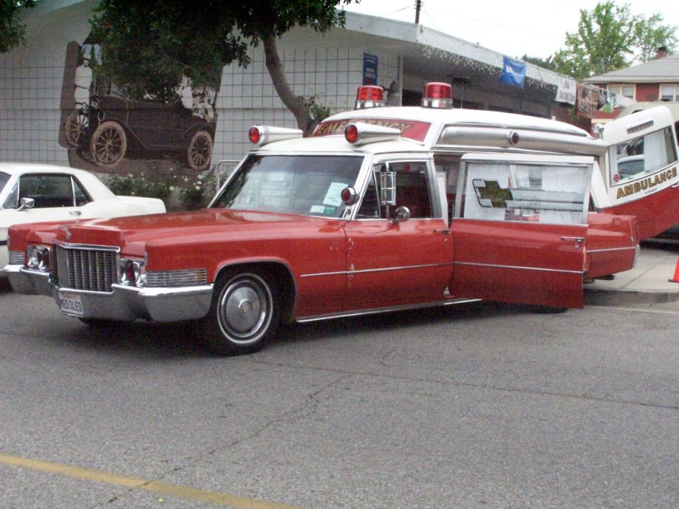 Red and white 1970 Cadillac ambulance with roof beacons parked at a car show