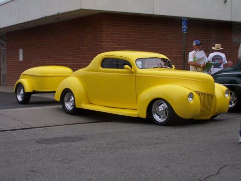 1990 Ford Bronco - A bright yellow coupe from the 1940s, complete with a matching custom trailer, is displayed at a car show.