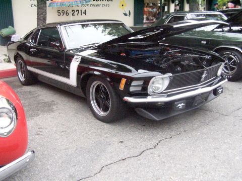 1990 Ford Bronco - Black 1970 Ford Mustang Boss 302 at a car show, hood open, parked beside a green Chevrolet Chevelle SS.
