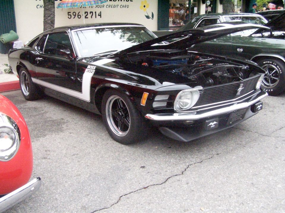 Black 1970 Ford Mustang Boss 302 with hood open, parked next to a green Chevrolet Chevelle SS