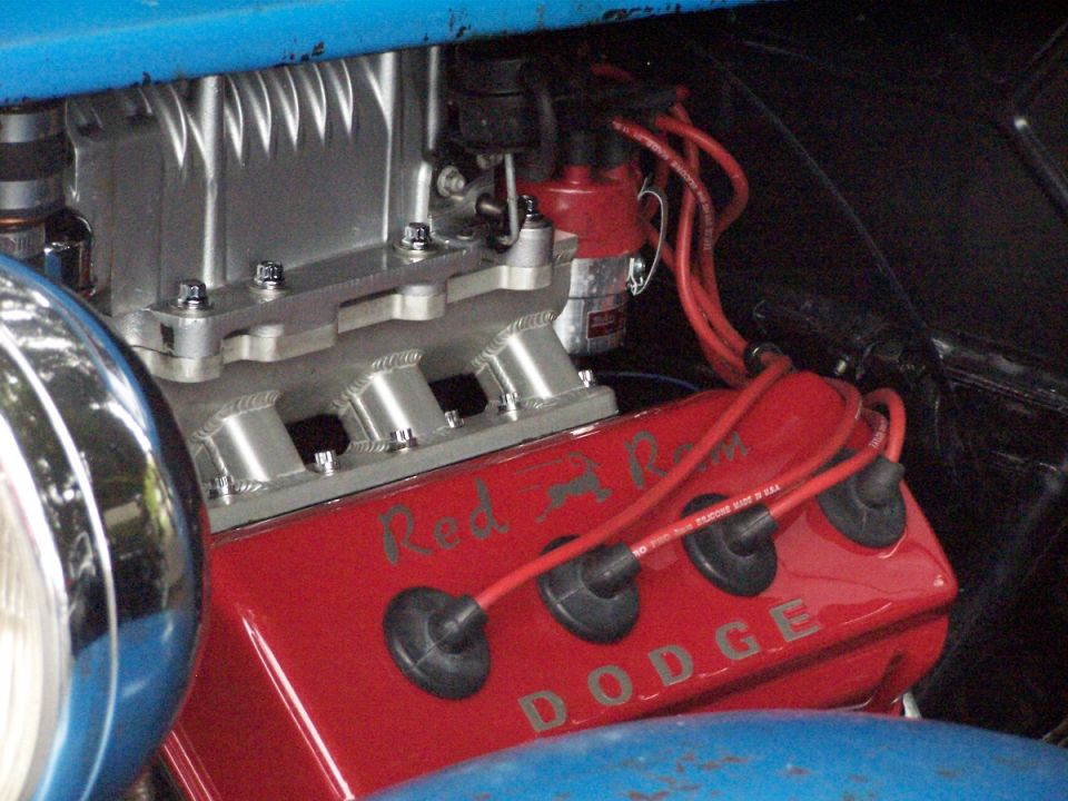 Close-up of a red Dodge engine with "Red Ram" and "DODGE" lettering. Silver intake manifold and red spark plug wires are visible
