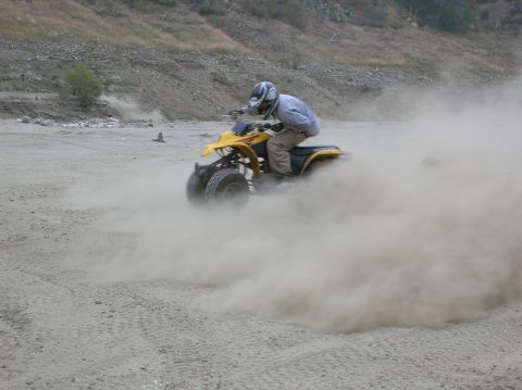 1985 Ford Bronco - Rider on a yellow quad bike drifts on a dusty dirt track, creating a large plume of dust.