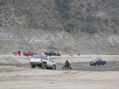 1985 Ford Bronco - Multiple vehicles and people are enjoying off-road activities on a sandy landscape with a large rocky hill.