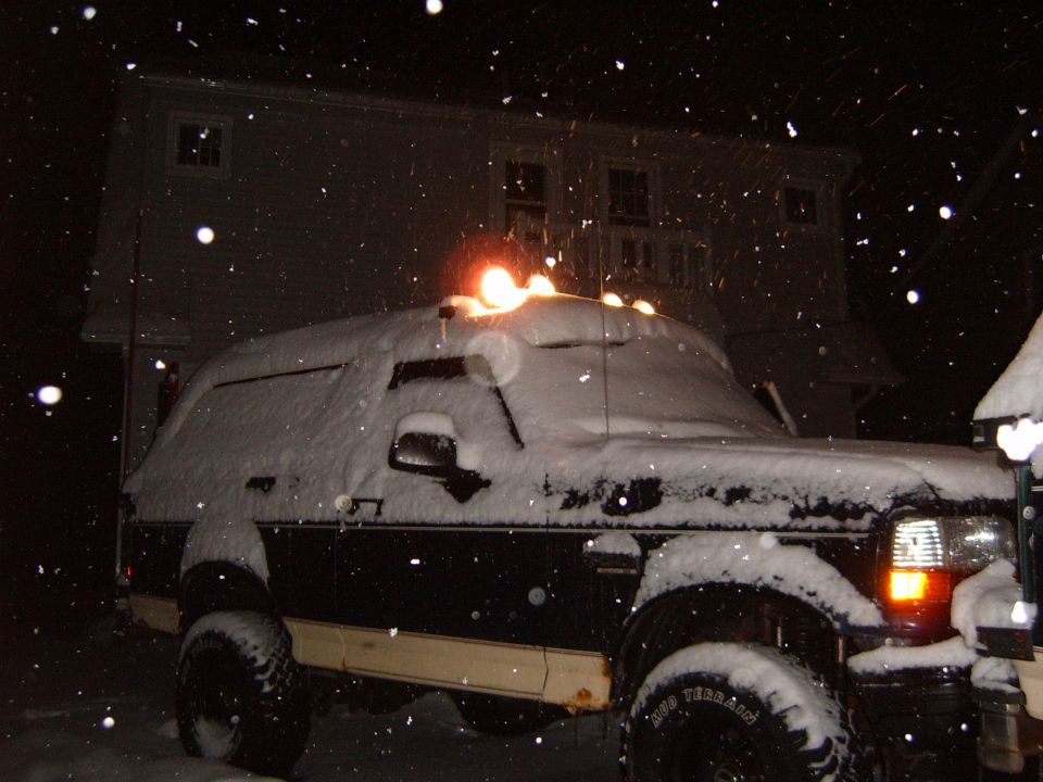1993 Ford Bronco covered in snow at night, parked in front of a house