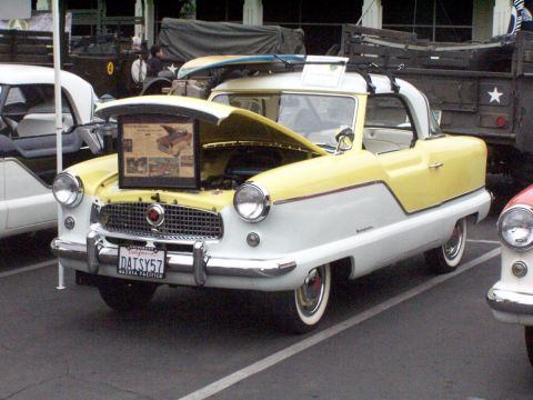 1990 Ford Bronco - A vintage Nash Metropolitan is displayed with its hood open, showing a surfboard on its roof.