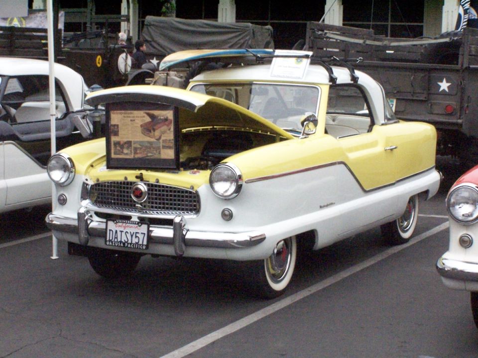 Yellow and white Nash Metropolitan with hood open, surfboard on roof, license plate DAISY57