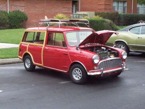 1990 Ford Bronco - A red woody wagon with a surfboard on its roof rack is parked next to another car, its hood open.