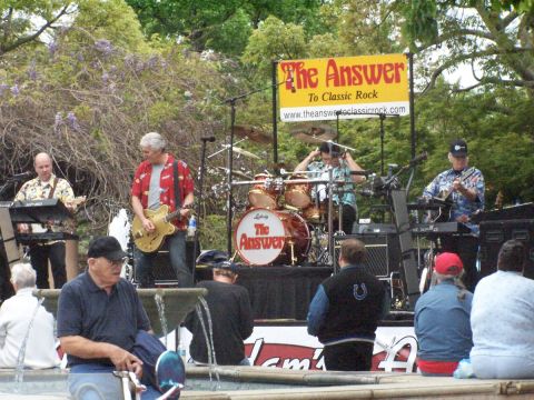 1990 Ford Bronco - A band plays music on an outdoor stage in front of a banner advertising their classic rock performance.