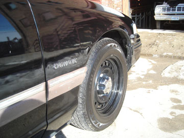 1992 Ford Crown Victoria - Close-up of the front fender and wheel of a black sedan, with another vehicle parked in a garage behind it.