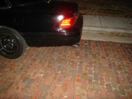 1992 Ford Crown Victoria - Rear view of a black 1992 Ford Crown Victoria sedan parked on a brick surface at night.