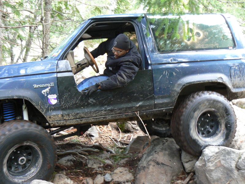 Driver in a blue 1986 Ford Bronco II navigating rocks on a trail