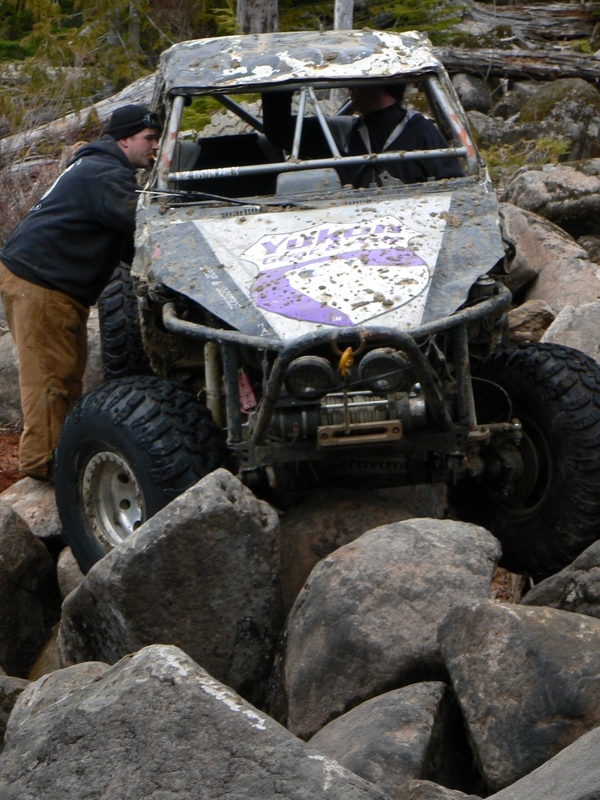 Mud-covered off-road vehicle with purple graphics navigating large rocks