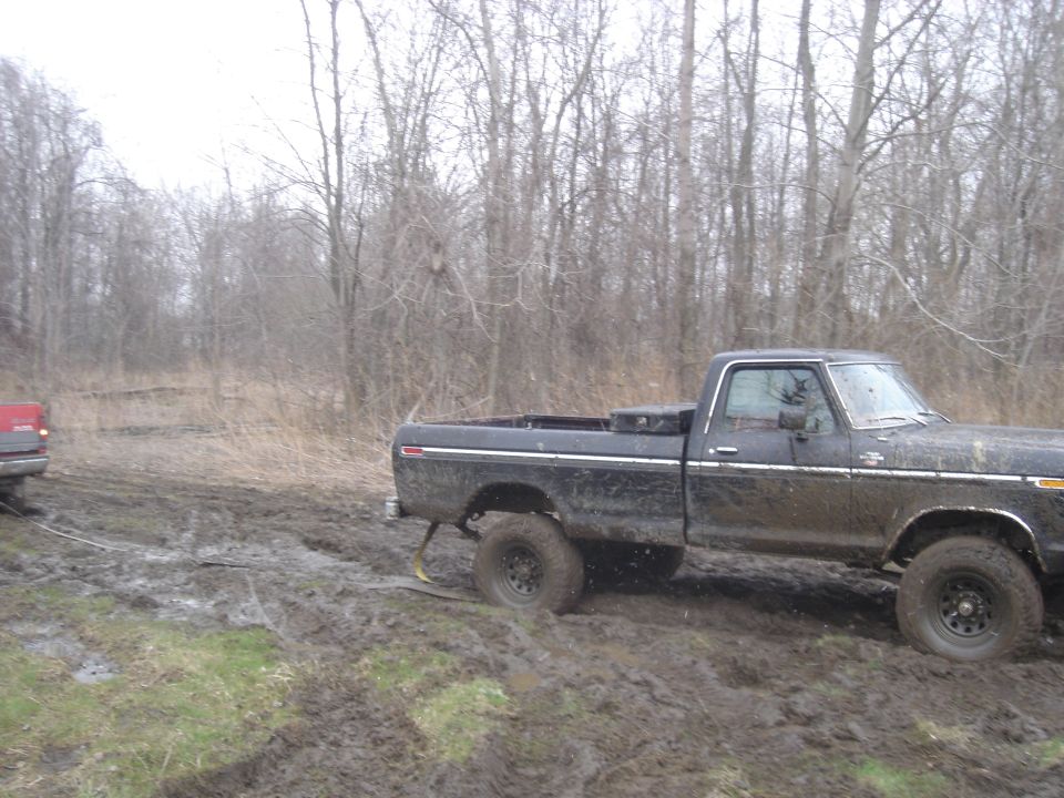 Black 1979 Ford F-250 stuck in mud, side view, with a red vehicle in the background also stuck